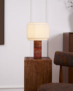 The hexagonal-shade lamp from Clérachic lit on a wood block, shown wider to reveal its full red travertine column.