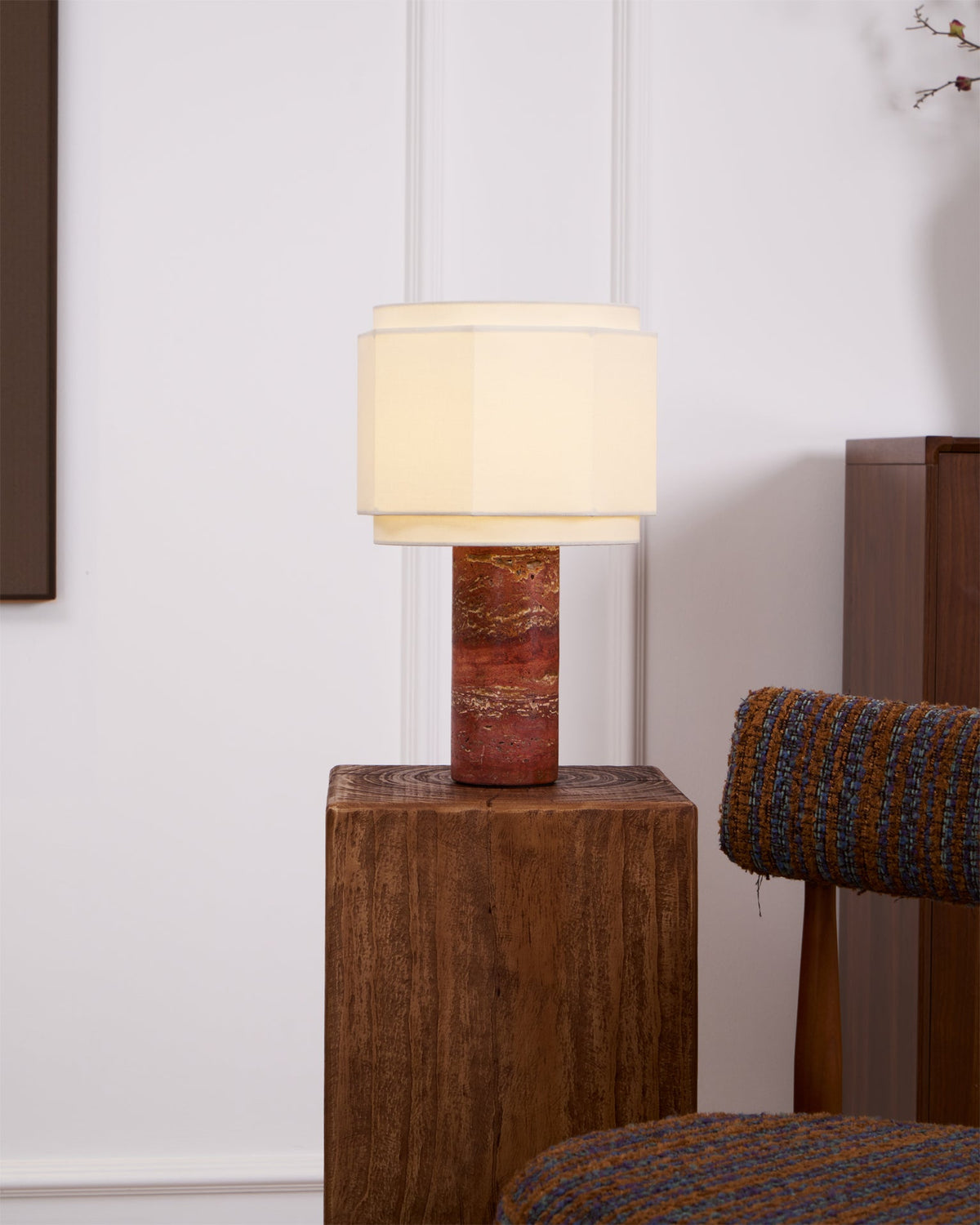 The hexagonal-shade lamp from Clérachic lit on a wood block, shown wider to reveal its full red travertine column.