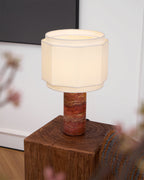This Clérachic table lamp glows on a wood plinth beside a blurred cherry-blossom branch and dark framed artwork.