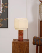 The table lamp from Clérachic lit in a narrow crop, framed art to the left and a blossom branch and vase to the right.