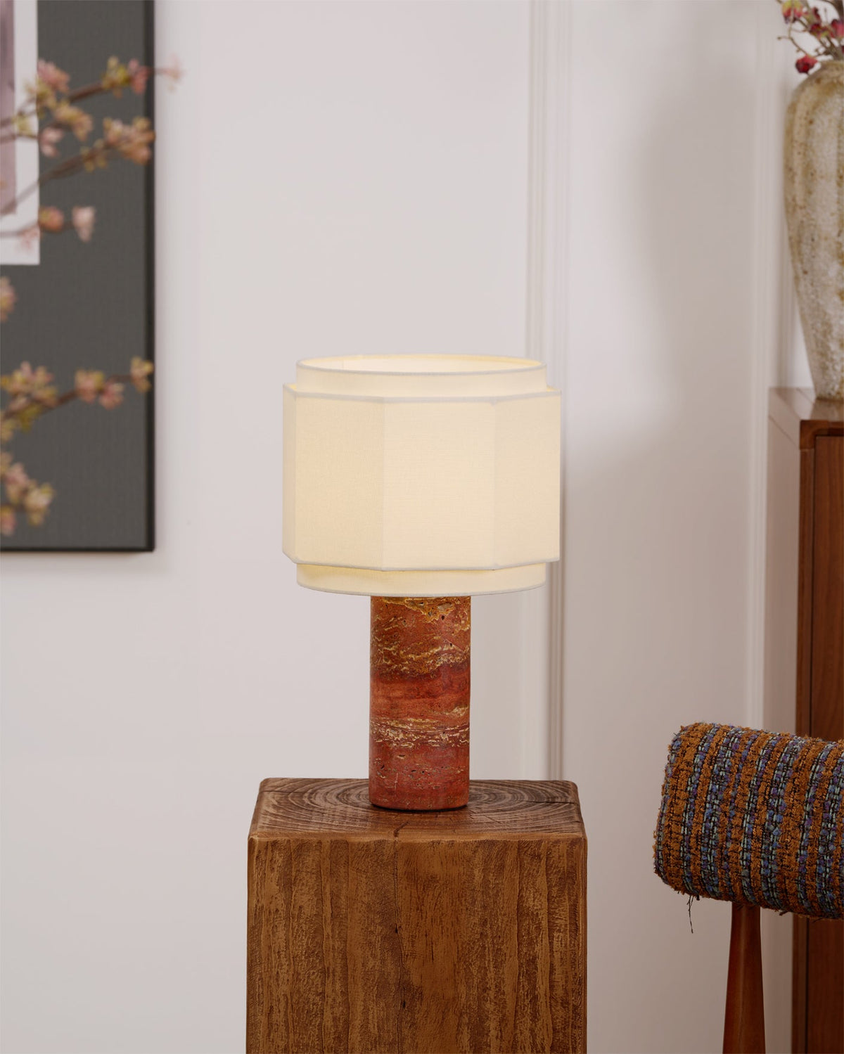The table lamp from Clérachic lit in a narrow crop, framed art to the left and a blossom branch and vase to the right.