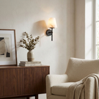 In matte black, this Clérachic wall light hangs above a wood sideboard with a framed print and a stoneware vase.