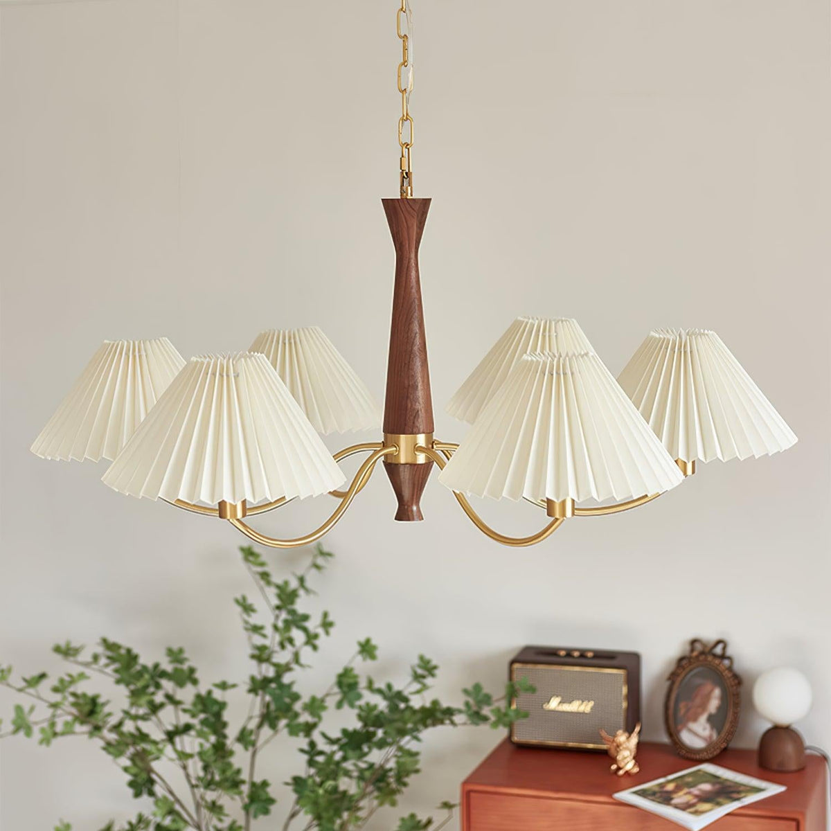 Ivory pleated shades on this Clérachic chandelier glow softly above a rust dresser, framed photo and potted greenery.