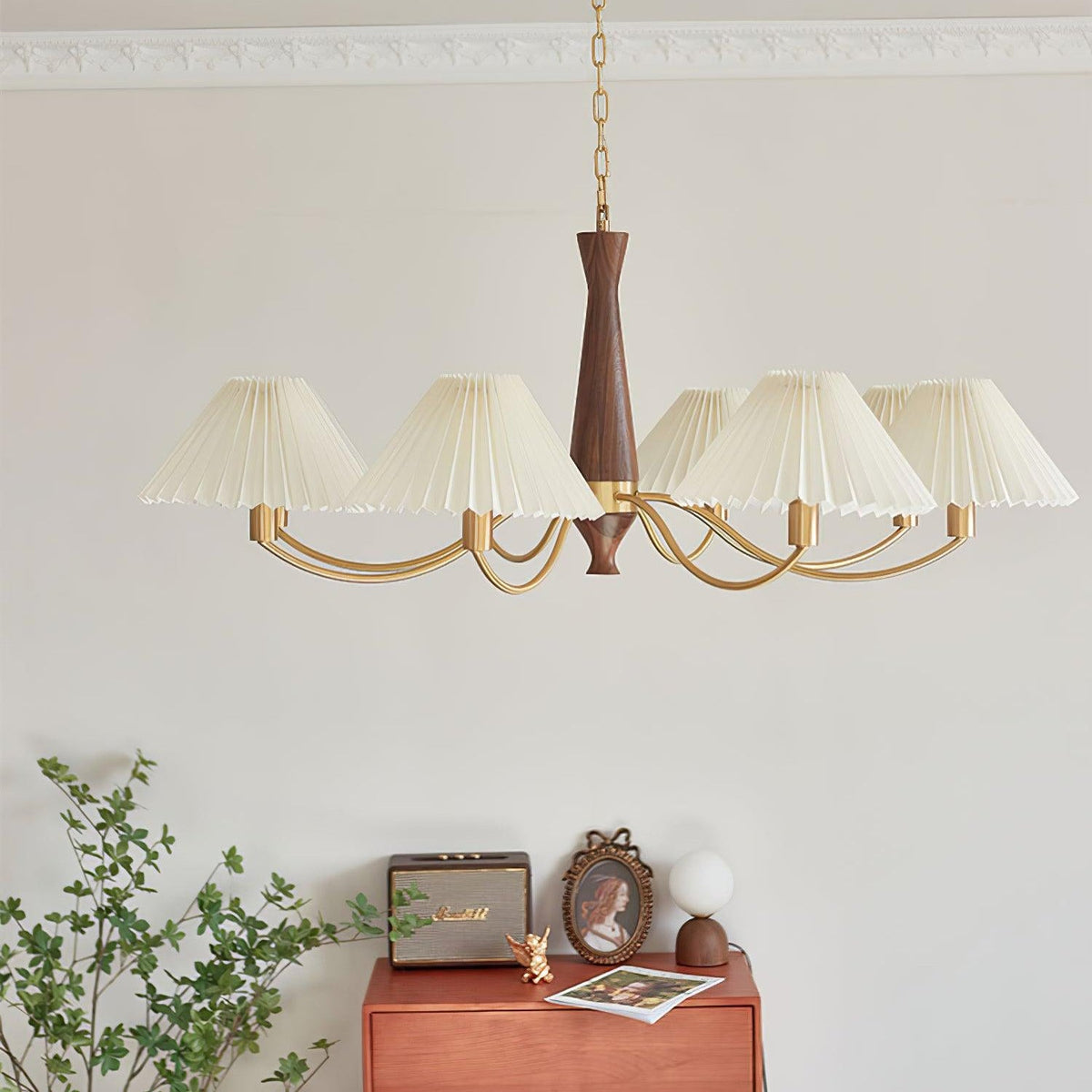 A full arc of pleated shades on this Clérachic chandelier hangs low over a rust-coloured dresser and framed photograph.