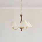 Three ivory pleated shades cluster around the walnut column of this Clérachic chandelier on a plain grey backdrop.