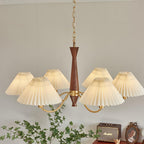 A wide arc of pleated shades cascades from this Clérachic chandelier above a dresser topped with a framed portrait and plant.