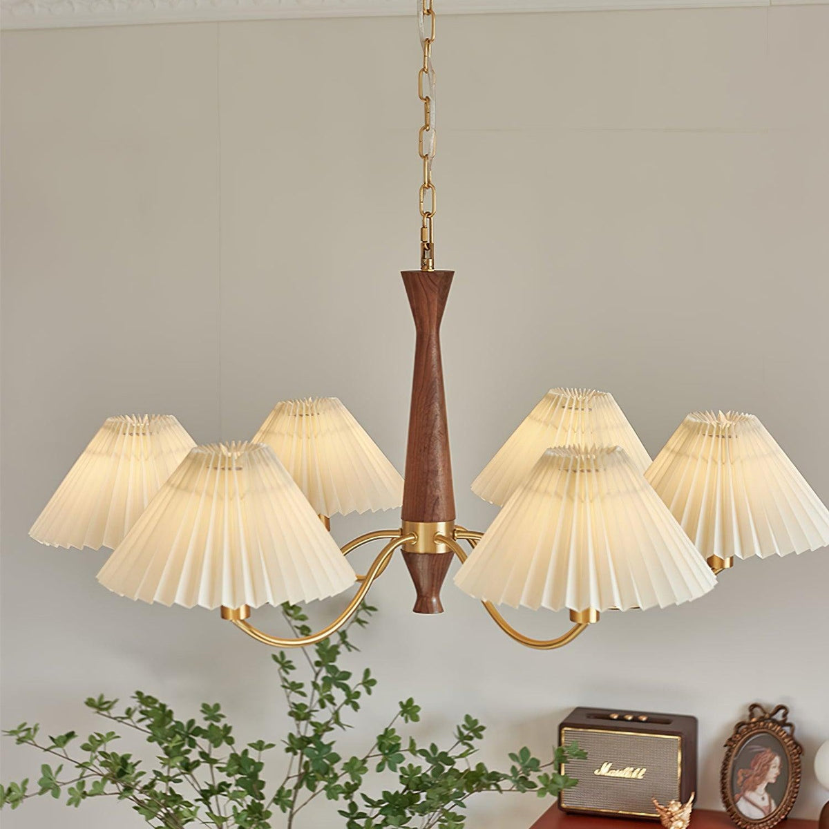 A wide arc of pleated shades cascades from this Clérachic chandelier above a dresser topped with a framed portrait and plant.
