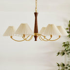 Trailing green leaves sit beside this Clérachic chandelier's row of pleated shades on a plain grey backdrop.