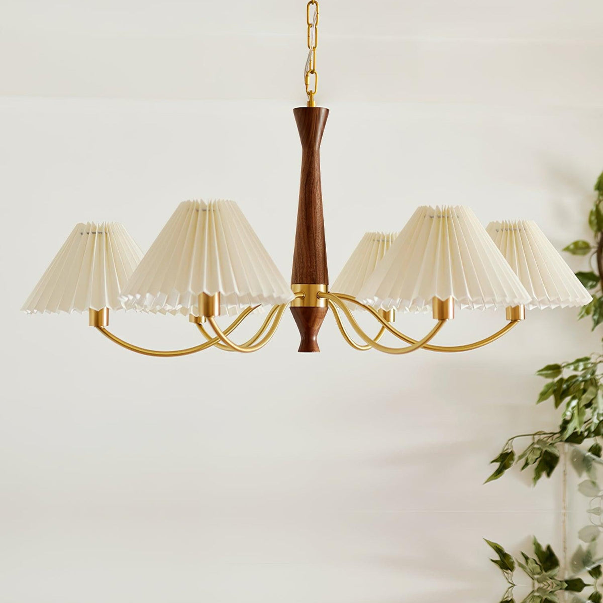 Trailing green leaves sit beside this Clérachic chandelier's row of pleated shades on a plain grey backdrop.