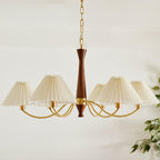 The walnut column of this Clérachic chandelier rises above its arc of pleated shades, with a leafy plant just visible at the edge.