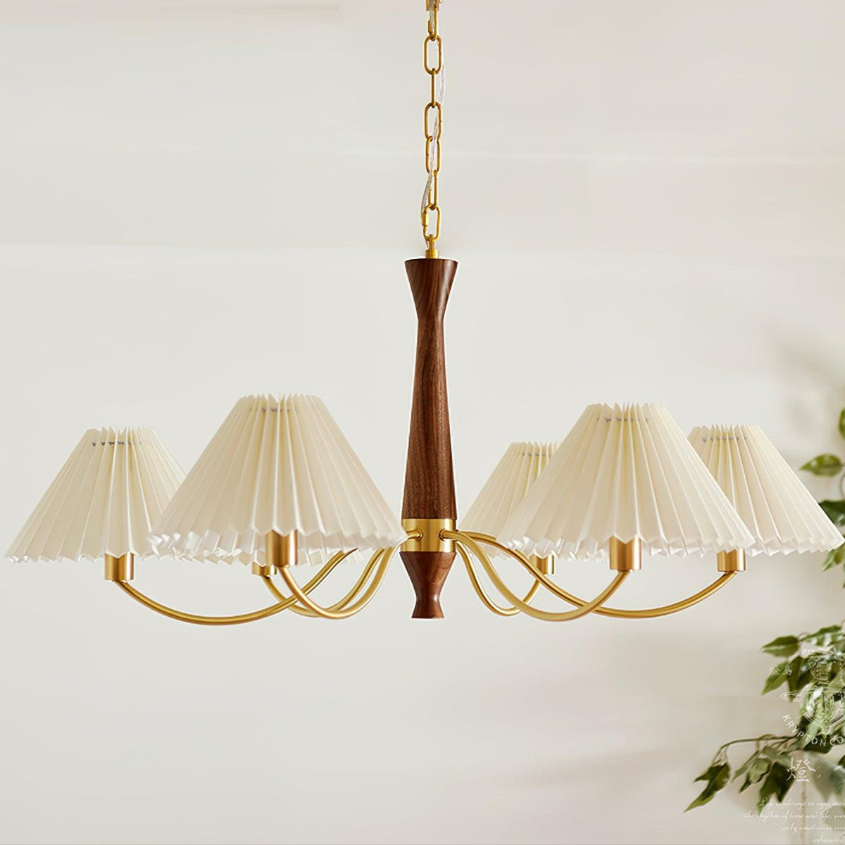 The walnut column of this Clérachic chandelier rises above its arc of pleated shades, with a leafy plant just visible at the edge.