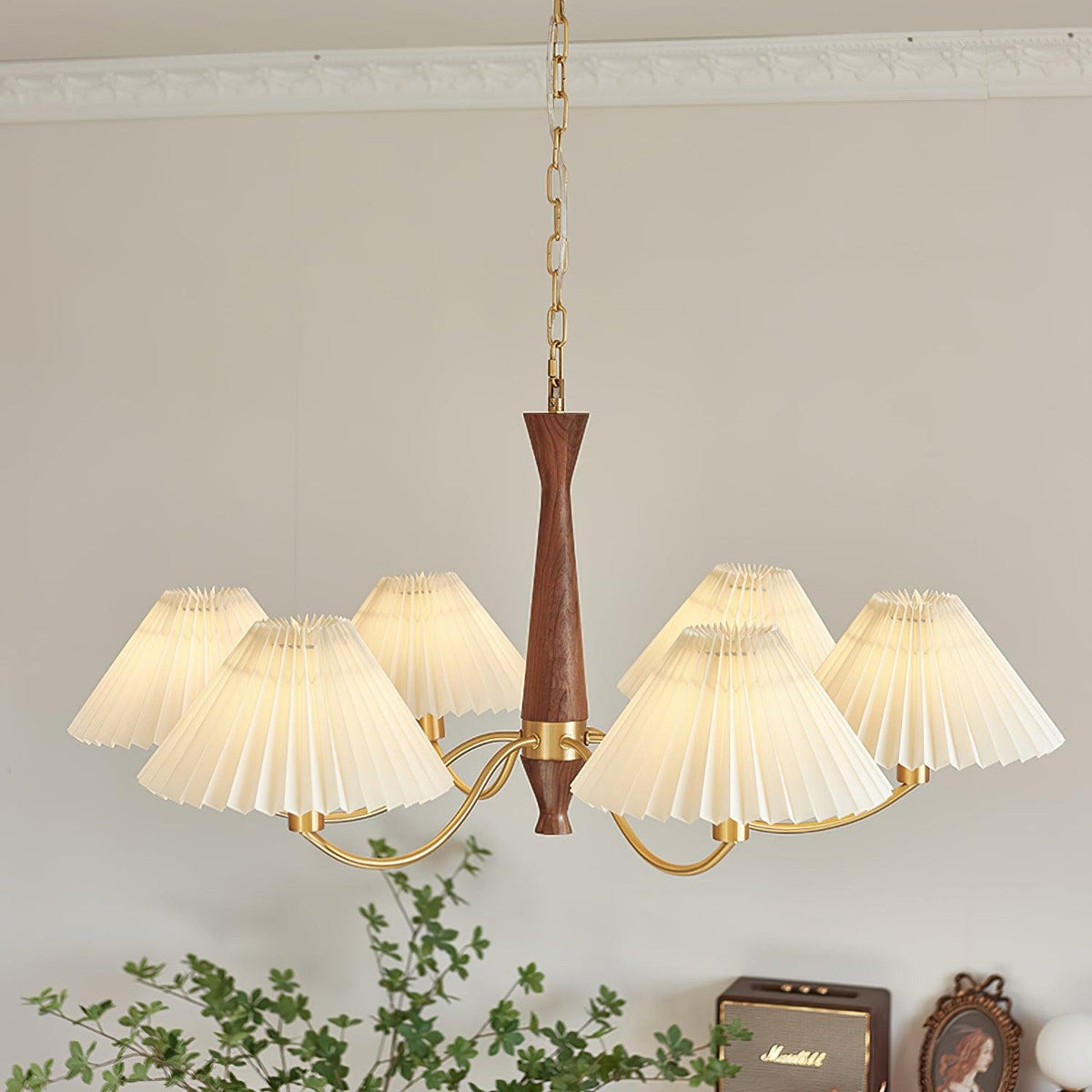 Ceiling moulding runs above this Clérachic chandelier, its pleated shades spread wide over a dresser and framed photo.