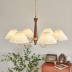 A sweeping arc of ivory pleated shades on this Clérachic chandelier hangs above a green plant and a rust-toned dresser.