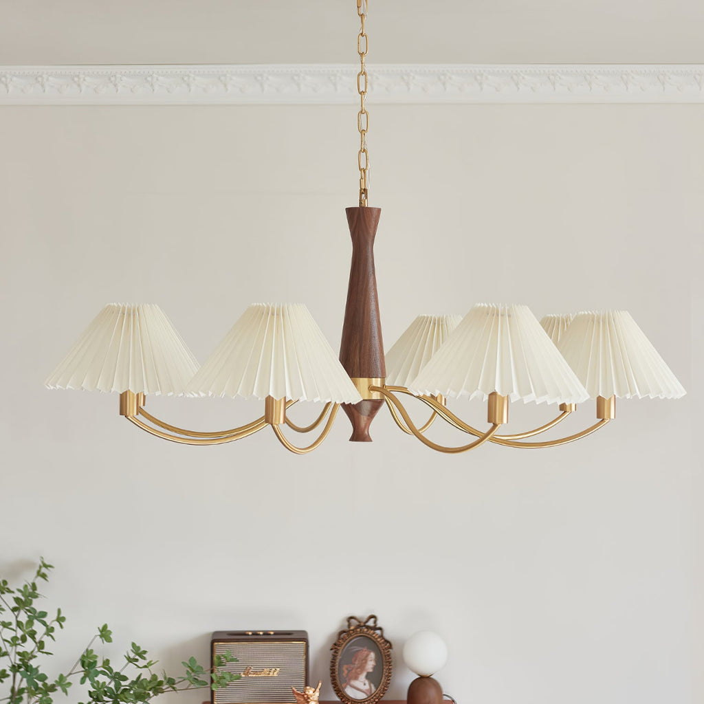 A wave of ivory pleated shades curves along brass arms on this Clérachic chandelier, shown against a plain grey wall.