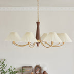 A wave of ivory pleated shades curves along brass arms on this Clérachic chandelier, shown against a plain grey wall.