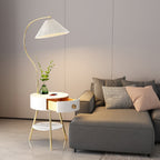 Seen from the other side, the Clérachic floor lamp's curved stem arches over the same white bedside table and grey sofa.