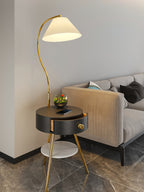 The black-and-brass Clérachic lamp holds a terrarium beside a beige sofa, its white marble shelf visible below.