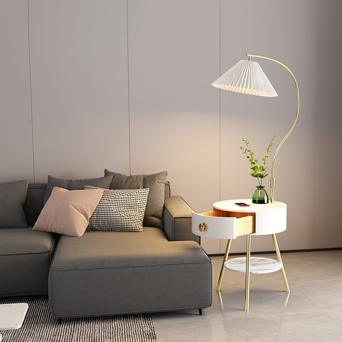 This Clérachic floor lamp's white built-in table sits beside a grey sofa, its pleated shade glowing on a curved brass stem.