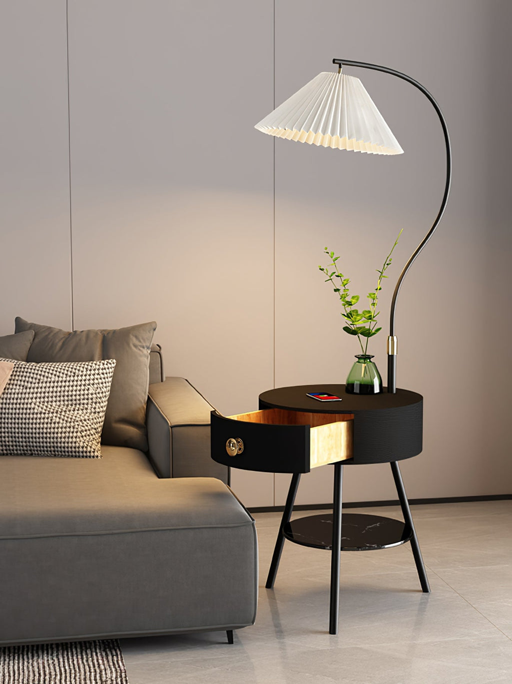 Beside the grey sofa, the black-and-brass Clérachic lamp's drawer sits open under a glass vase of greenery.