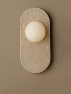 This travertine version of the Clérachic wall sconce is shown in a narrow crop, its pitted cream surface catching soft light.