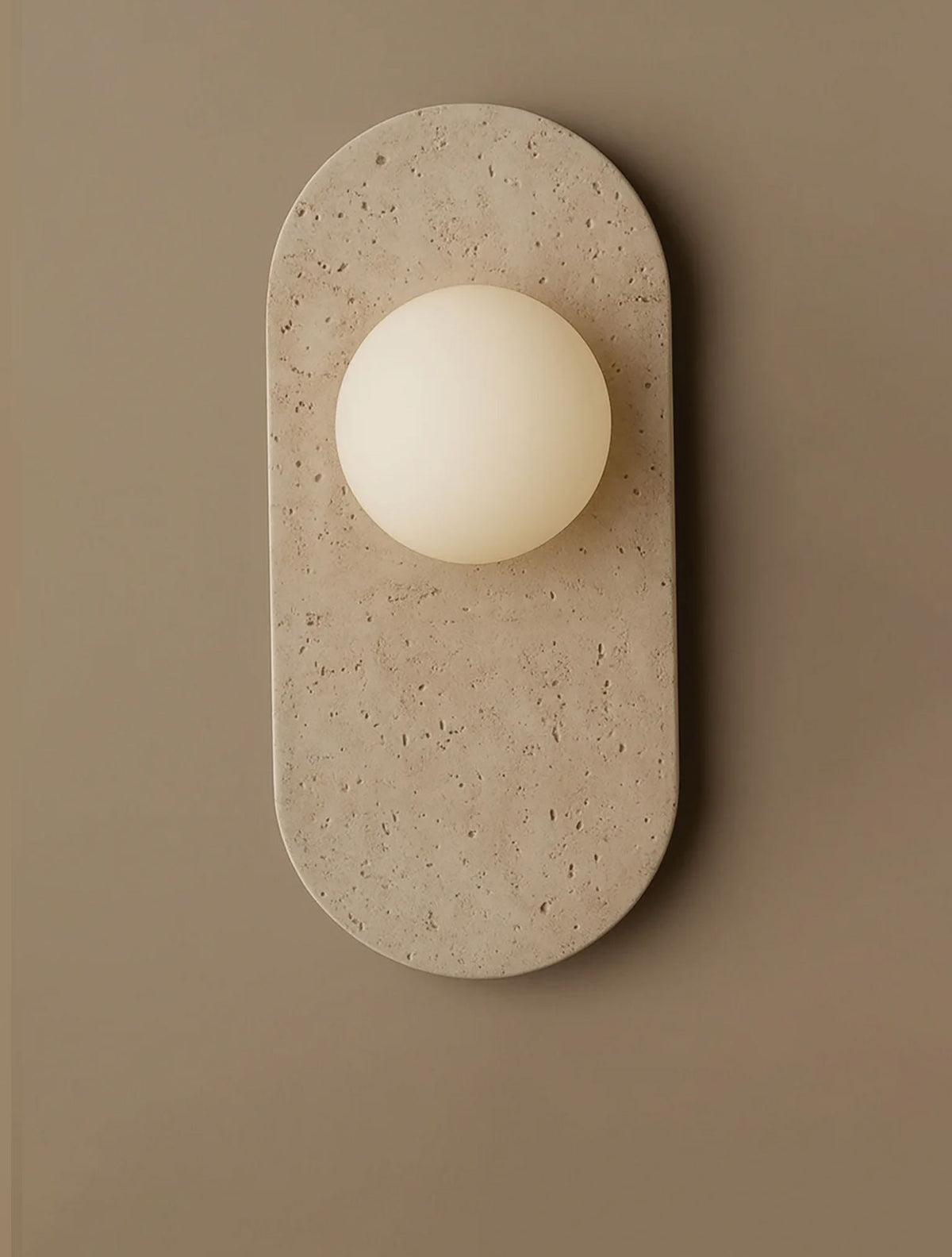 This travertine version of the Clérachic wall sconce is shown in a narrow crop, its pitted cream surface catching soft light.