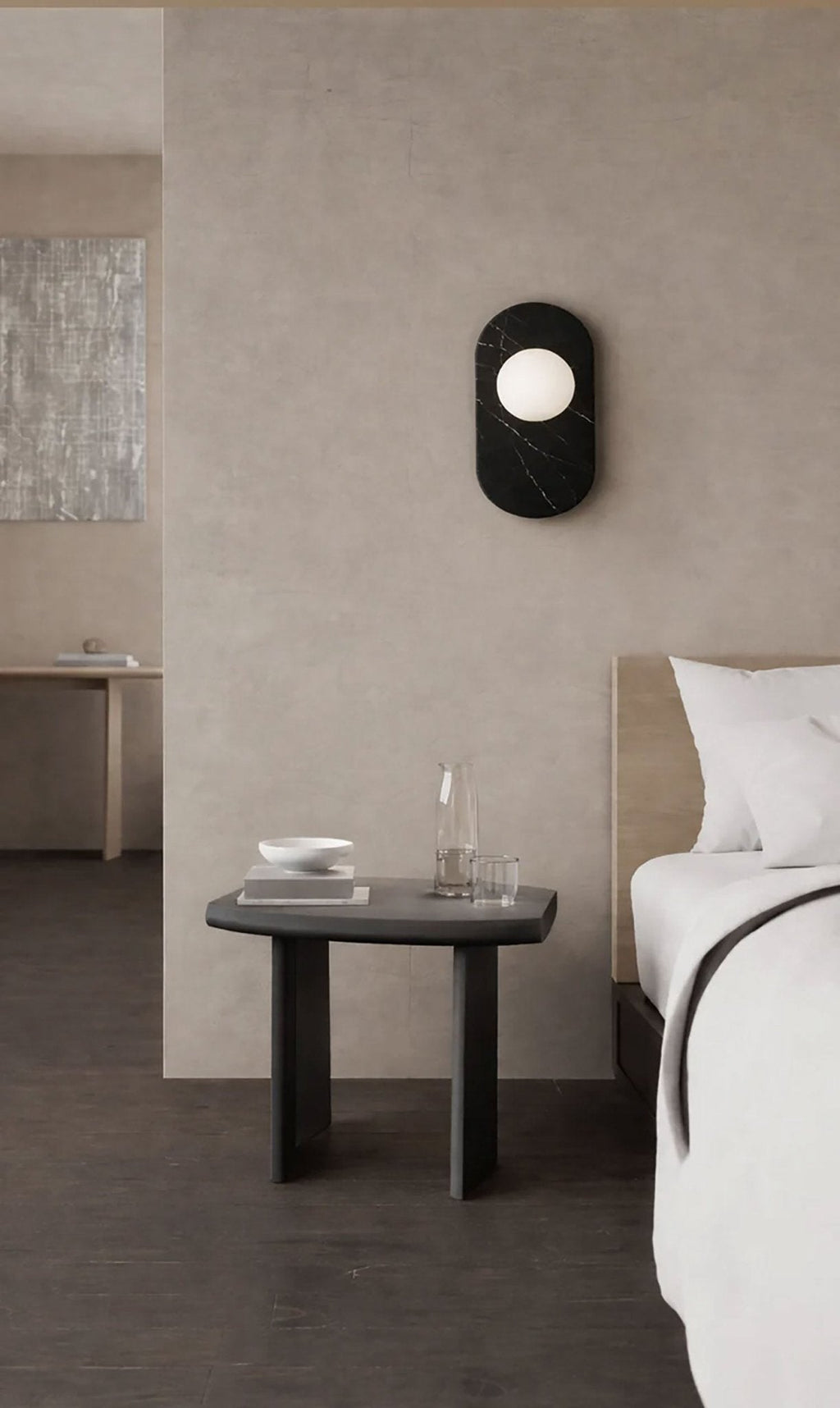Mounted above a dark bedside table set with a glass carafe and bowls, this Clérachic wall sconce lights a calm bedroom corner.