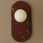 A closer view of the burgundy marble oval on this Clérachic wall sconce shows its natural white veining beside the glass globe.