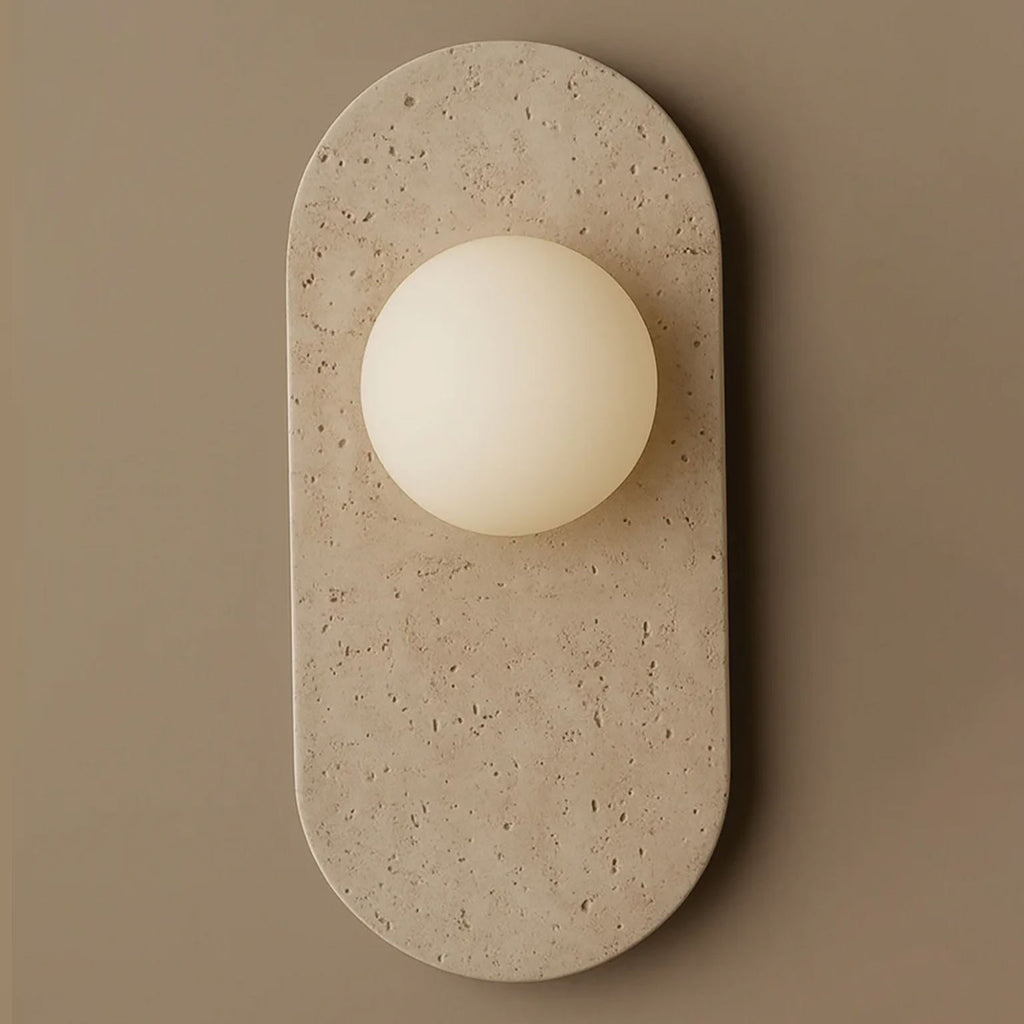 Cream travertine with natural surface pitting forms the oval body of this Clérachic wall sconce, shown close against a taupe wall.
