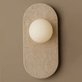 Cream travertine with natural surface pitting forms the oval body of this Clérachic wall sconce, shown close against a taupe wall.