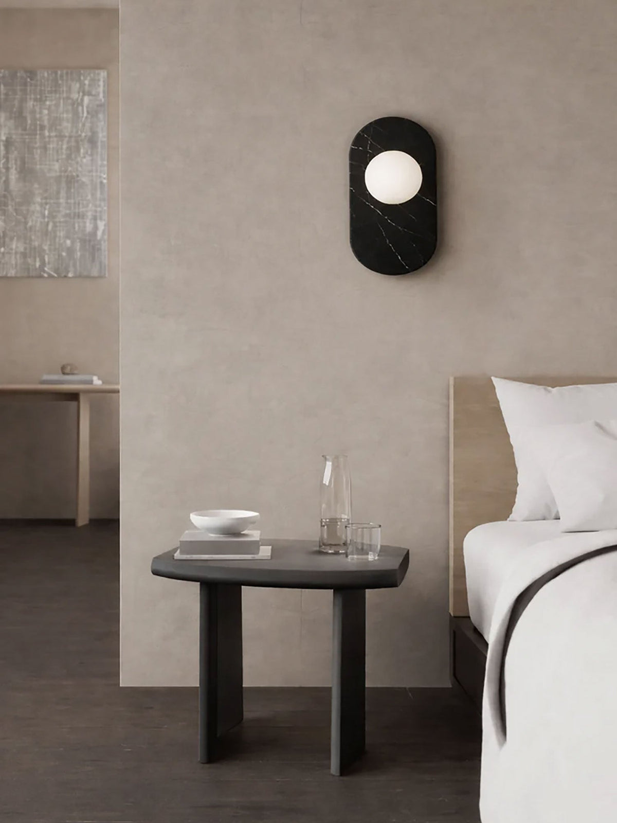 In this Clérachic bedroom scene, the black marble sconce lights the wall above a nightstand set with a carafe, near a framed print.