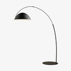Verse arc floor lamp with tapered black stem beside a reading chair