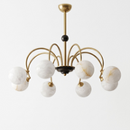 This brass Clérachic chandelier stands unlit on a plain white background, a small black accent marking where its arms meet.