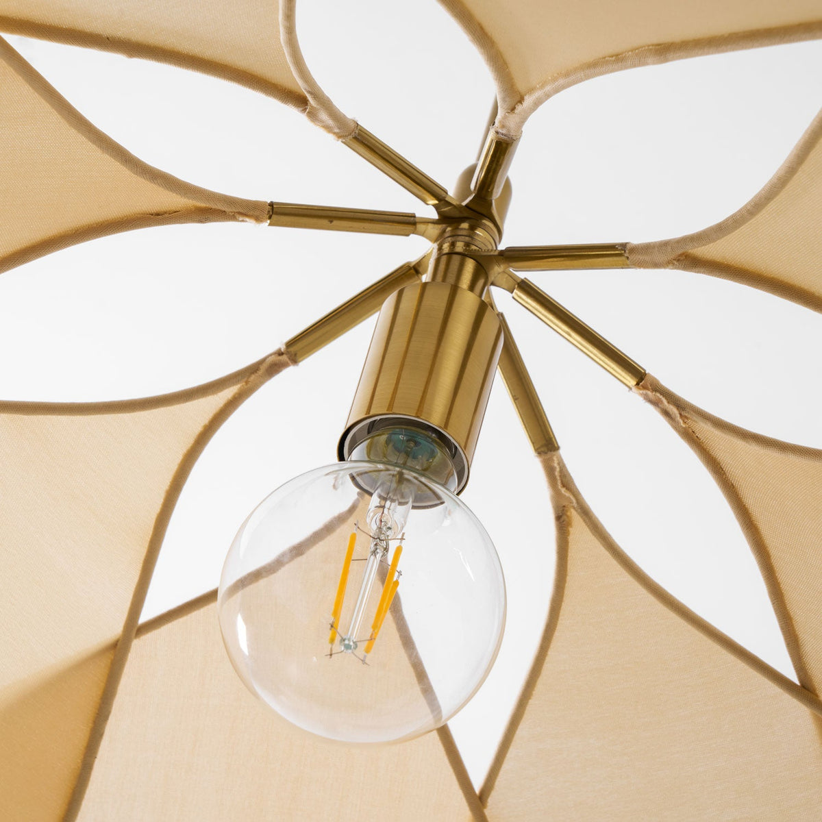 Close-up of this Clérachic pendant lamp's brass frame and exposed filament bulb, seen through its open fabric petals.