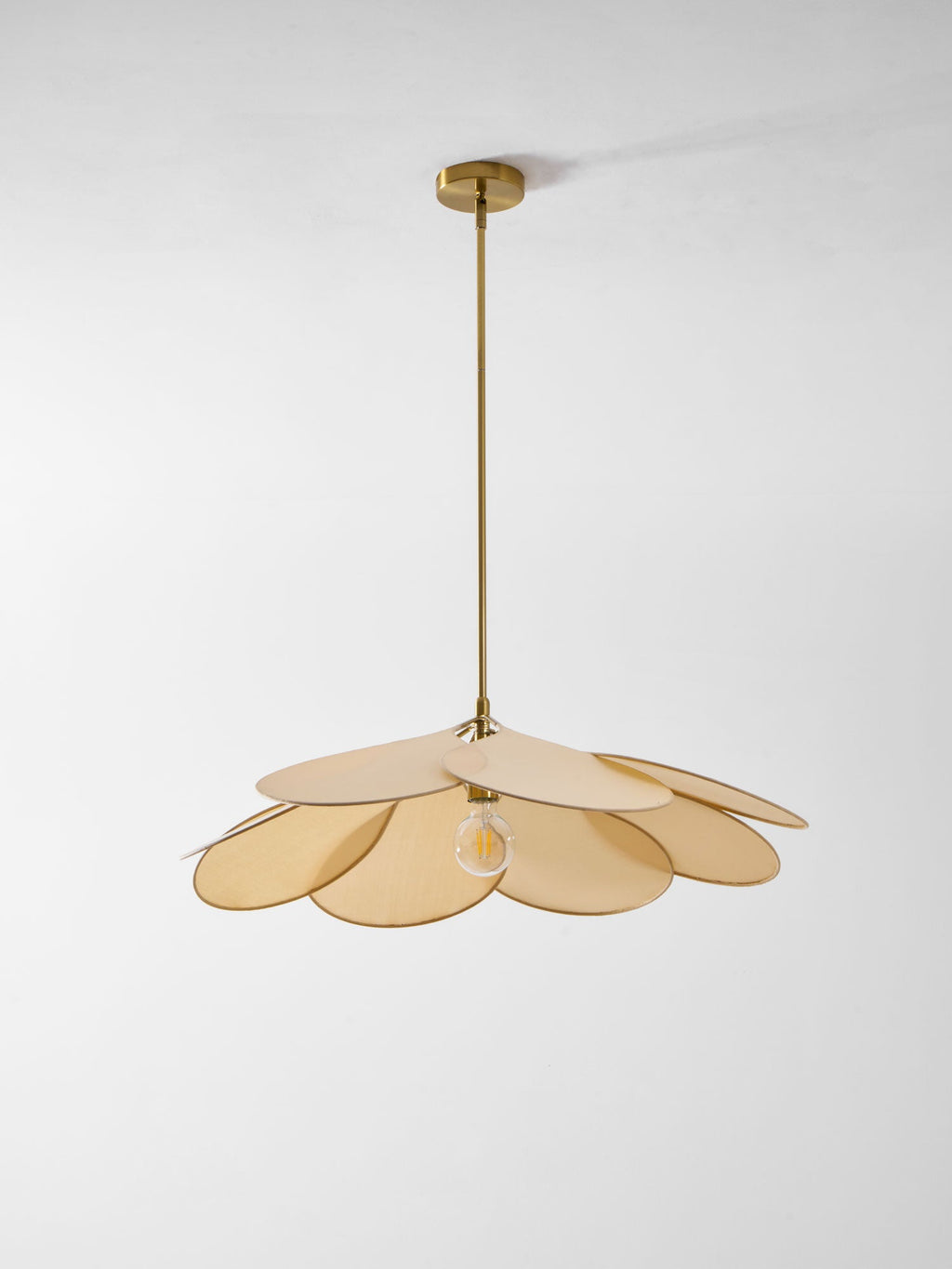 This Clérachic pendant lamp in beige petals hangs low against a plain grey background, its bulb glowing at the centre.