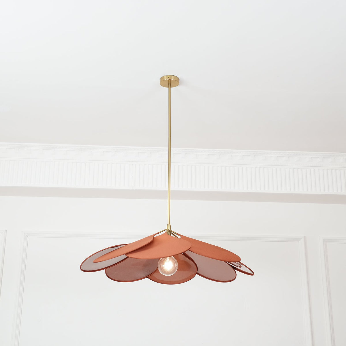 Centred in a panelled room, this Clérachic pendant lamp shows terracotta petals with its bulb glowing beneath.