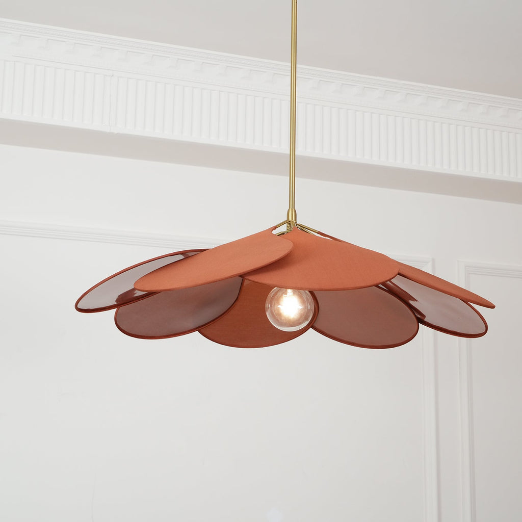This Clérachic pendant lamp's terracotta petals hang low on a long brass stem, its bulb glowing at the centre.