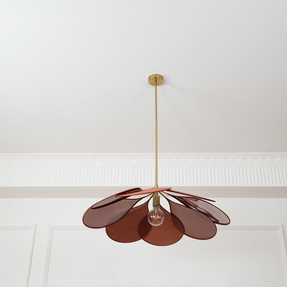This Clérachic pendant lamp in deep rust petals hangs low, its bulb glowing beneath the fanned shade.