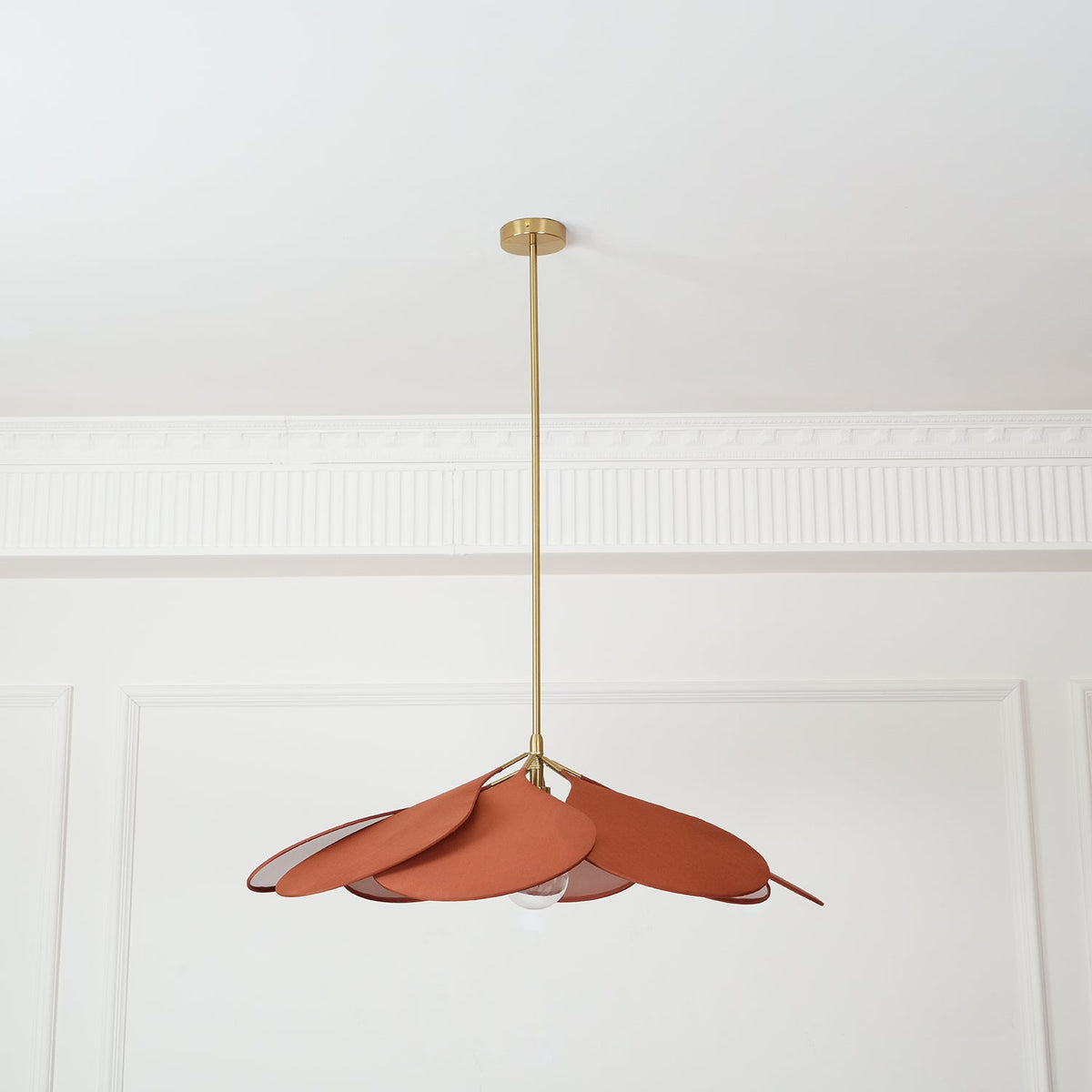 This Clérachic pendant lamp in terracotta petals hangs high on a long brass stem, splayed loosely to one side.