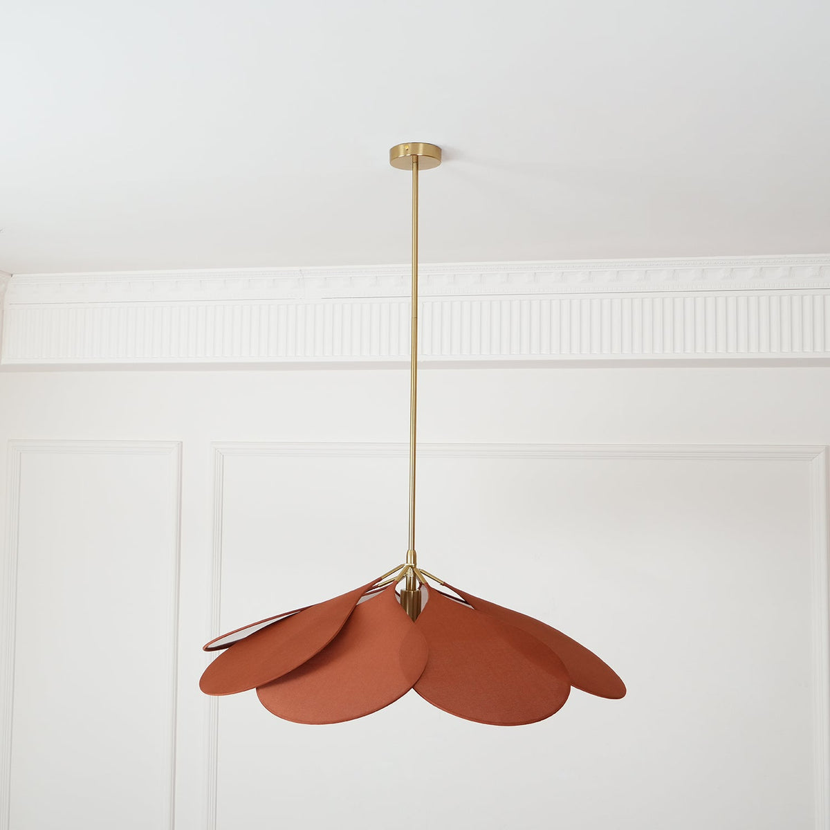 Hanging from a long brass stem, this Clérachic pendant lamp's terracotta petals sit above a plain panelled room.