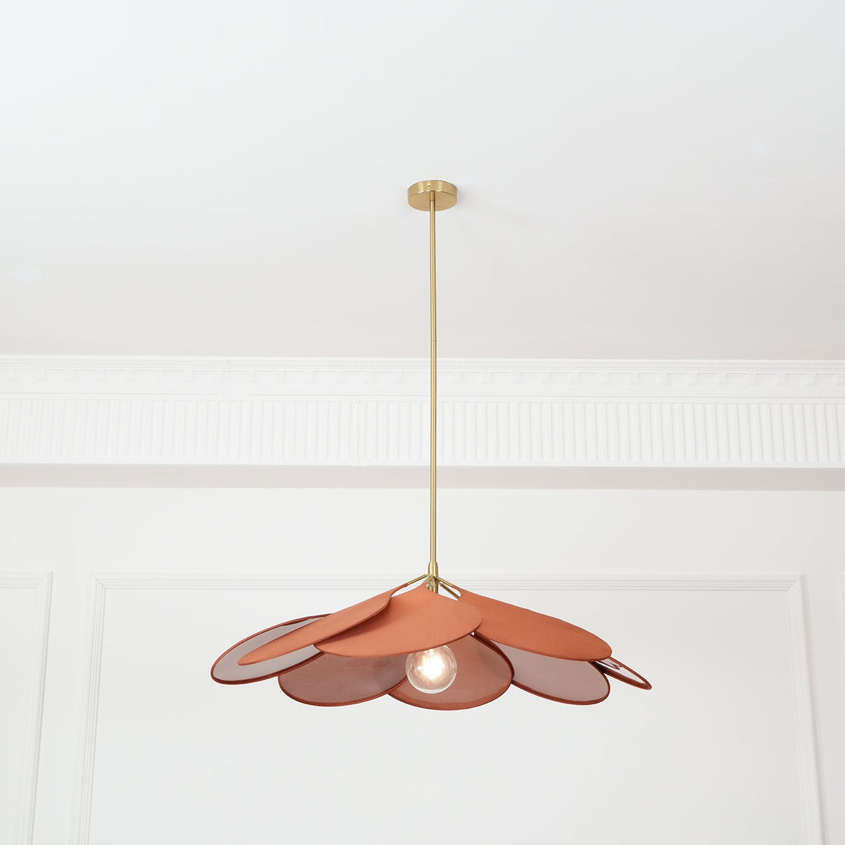 Studio shot of this Clérachic pendant lamp from below, its terracotta fabric petals fanned open around a glowing bulb on a brass stem.
