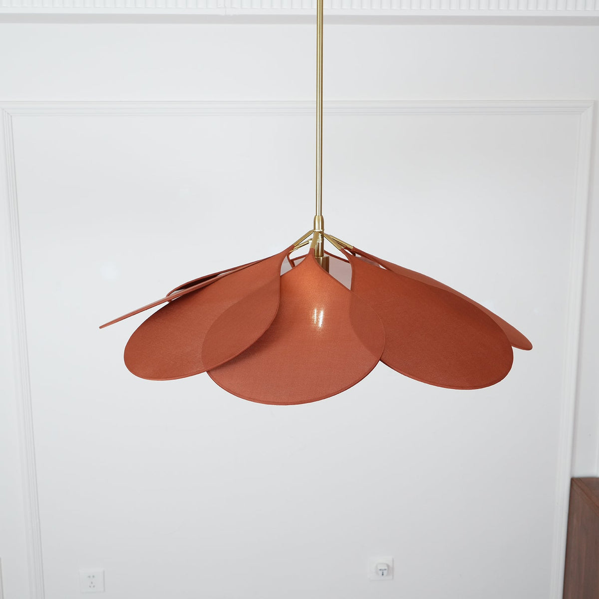 Close view from below of this Clérachic pendant lamp's terracotta petals, fanned unevenly against a plain wall.
