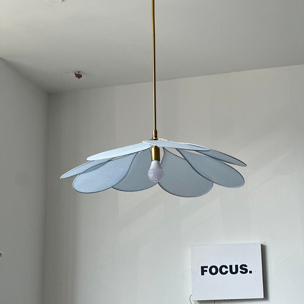 This Clérachic pendant lamp in pale blue petals hangs in a room corner near a white console and patterned cabinet.