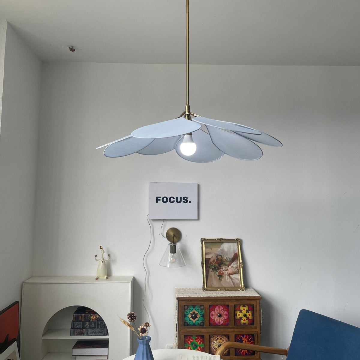 This Clérachic pendant lamp in pale blue petals hangs above a white console beside a patterned tile-front cabinet and a blue chair.