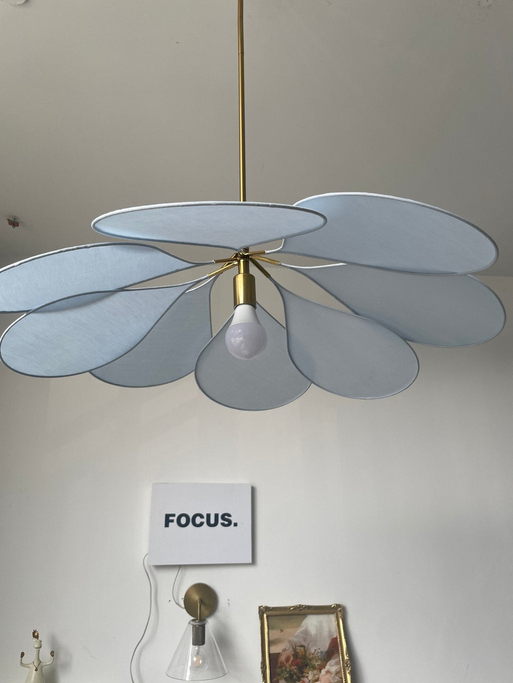 Close view of this Clérachic pendant lamp's pale blue petals and bulb, with a wall sconce visible behind.
