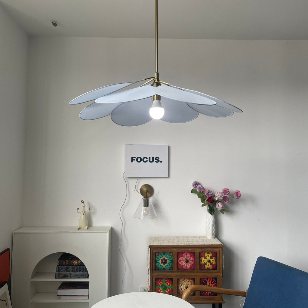 This Clérachic pendant lamp in pale blue petals hangs lit above a white console and a patterned cabinet with fresh flowers.