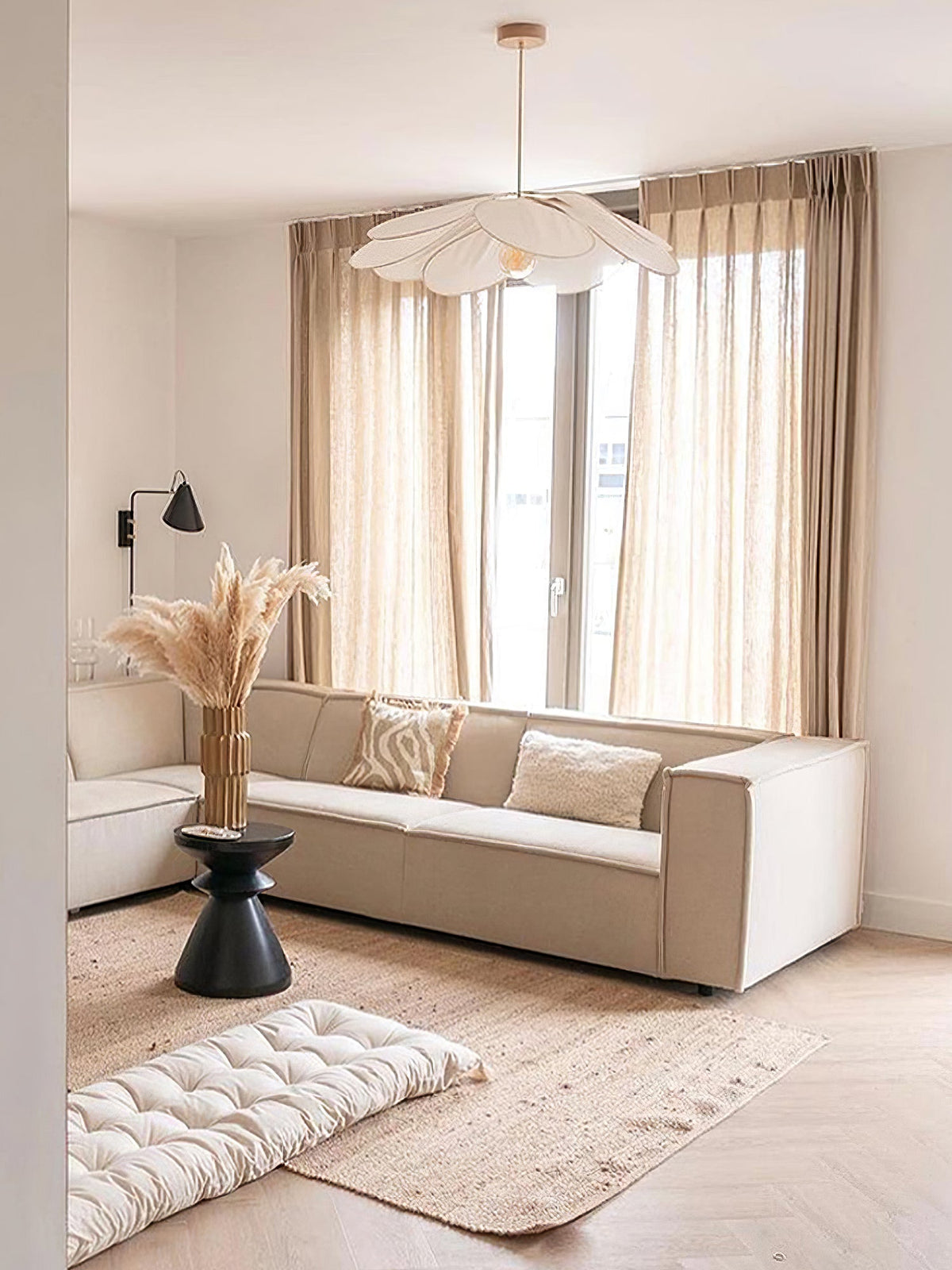 This Clérachic pendant lamp in cream petals hangs above a beige sofa in a living room with sheer curtains and a floor lamp.
