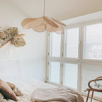 This Clérachic pendant lamp in tan petals hangs above a bed near louvred white shutters and a dried grass wall arrangement.