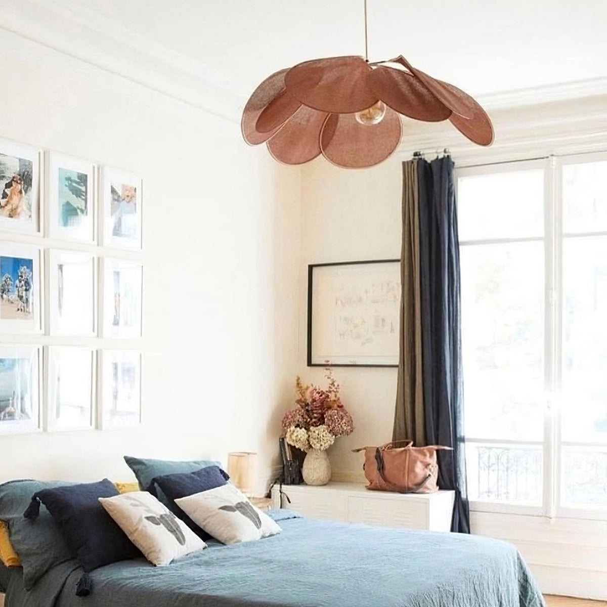 This Clérachic pendant lamp in wine-red petals hangs above a bed dressed in navy linen, beside tall windows with a dark curtain.