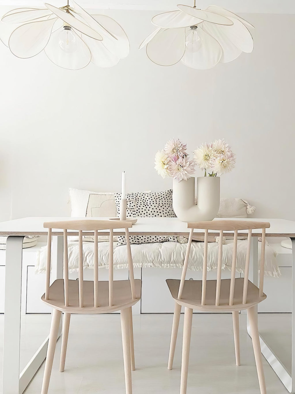 Two of these Clérachic pendant lamps in white petals hang above a white kitchen table with a built-in bench and fresh flowers.