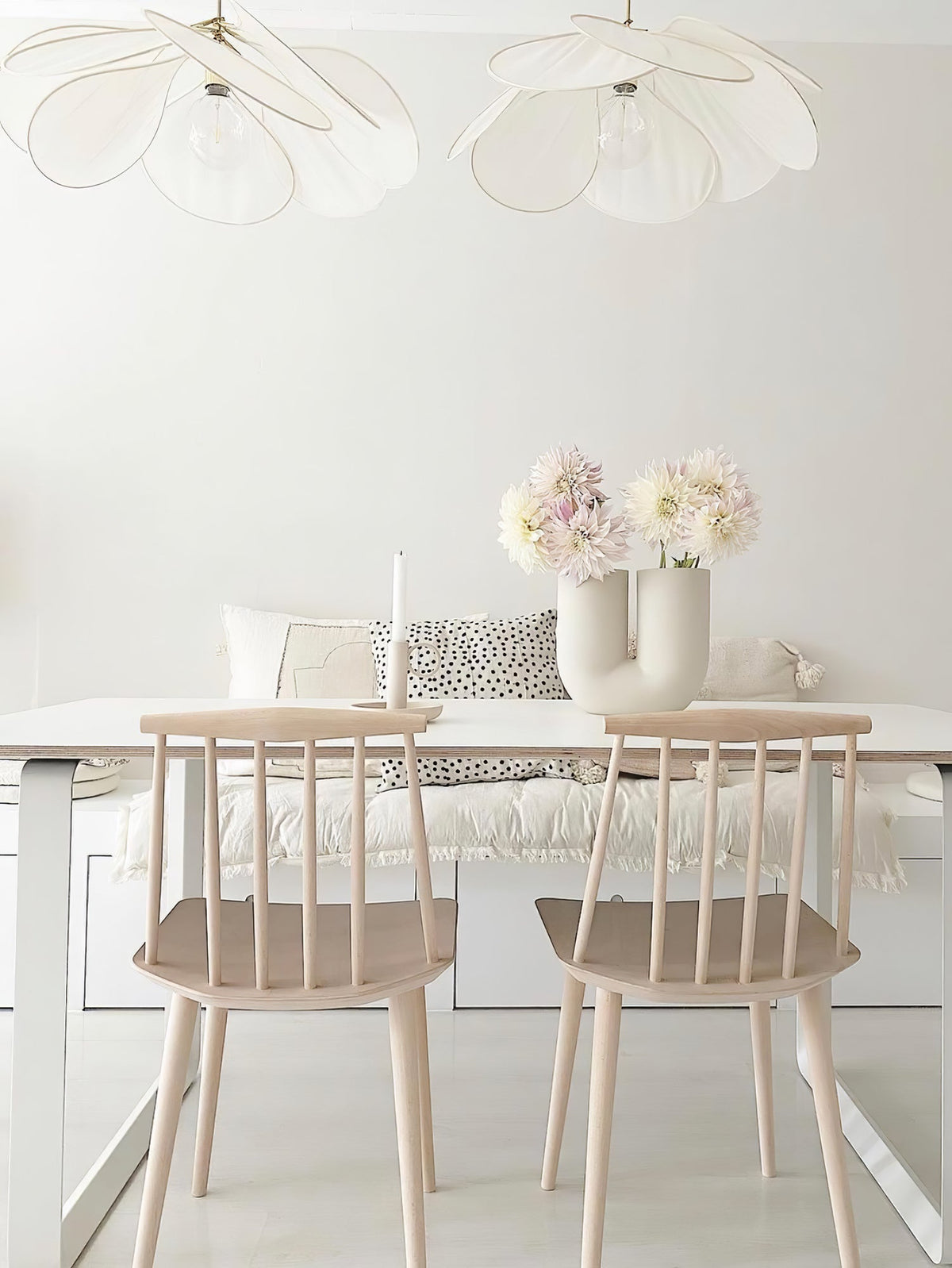 Two of these Clérachic pendant lamps in white petals hang above a white kitchen table with a built-in bench and fresh flowers.